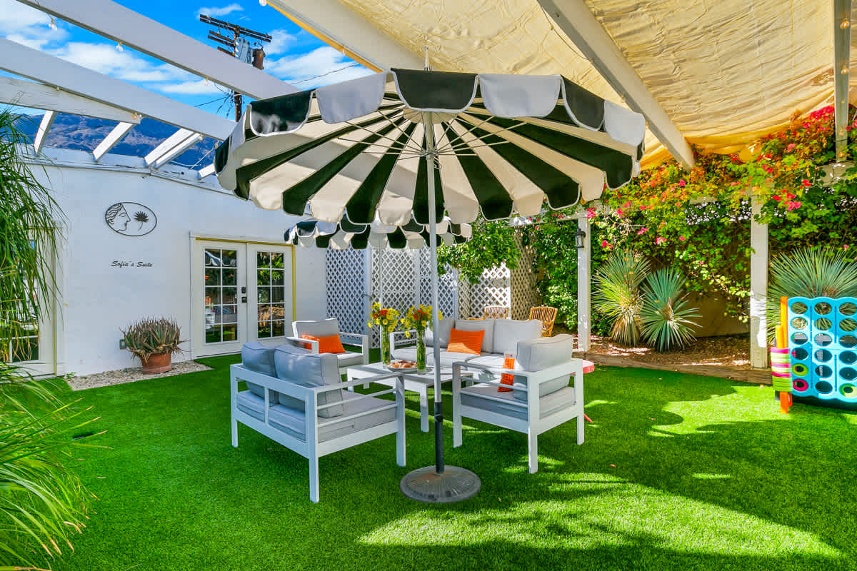 Shaded outdoor table and chairs surrounded by lawn and flowering plants.