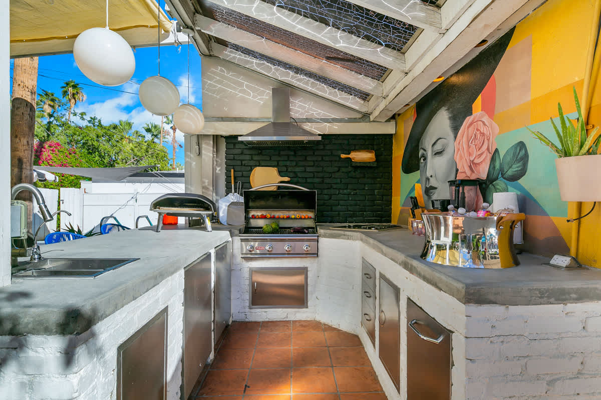 Covered outdoor kitchen with a grill, counters, sink and white cabinetry.