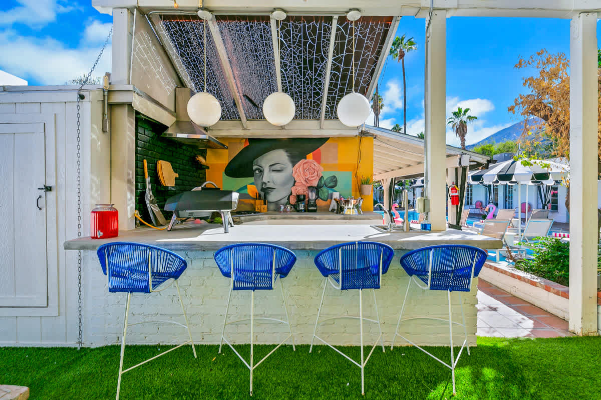 Outdoor kitchen and bar counter with blue-and-white stools beneath a pergola.