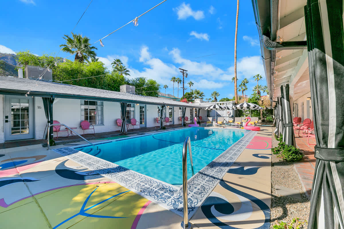 Pool and colorful deck viewed from beside the striped exterior awning.
