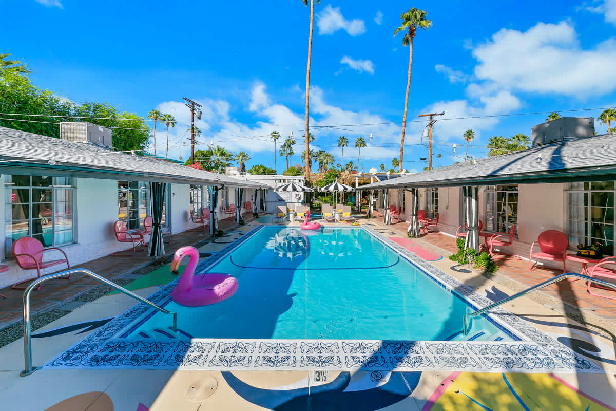 Wide courtyard pool view framed by palm trees and poolside rooms.