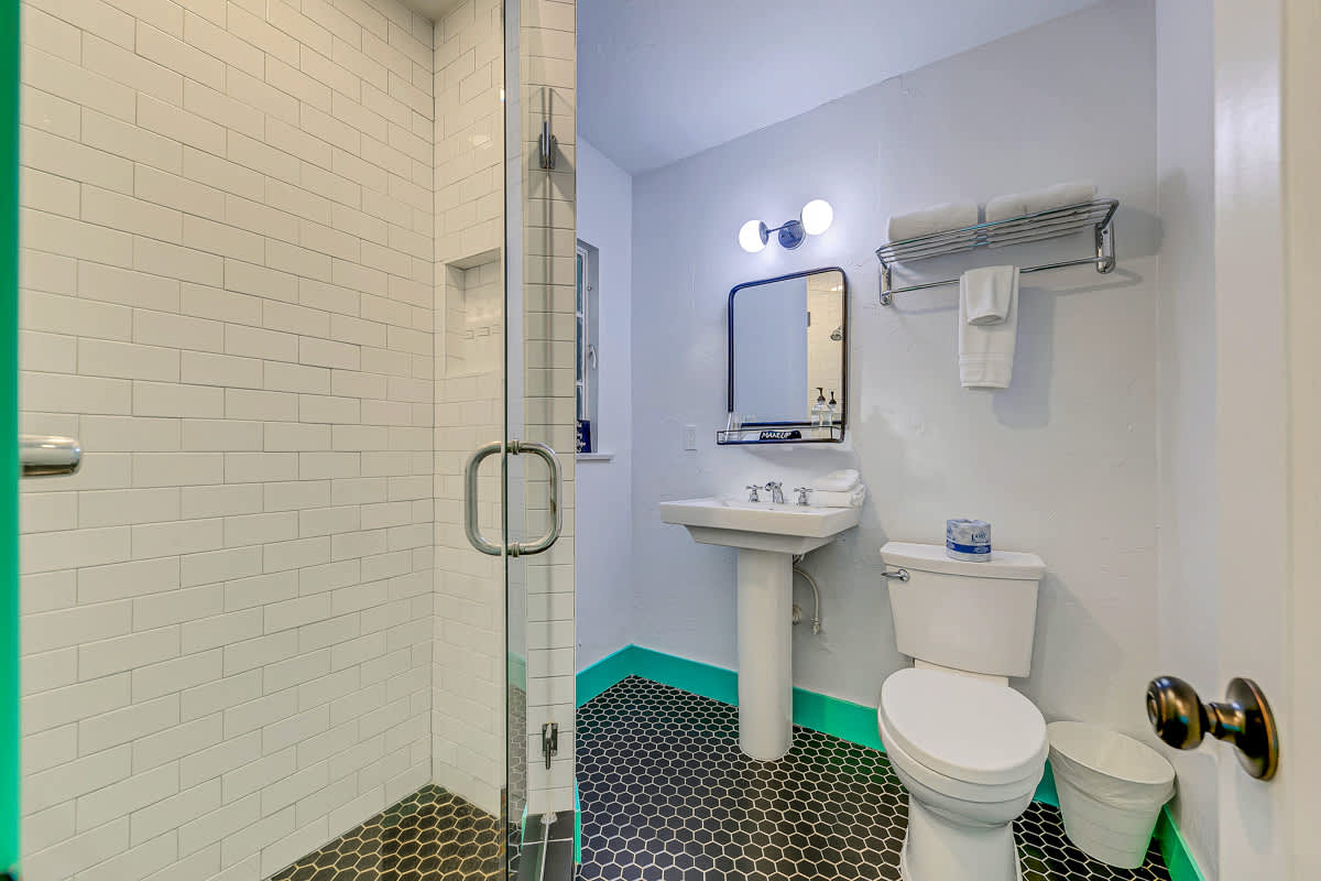 White bathroom with a pedestal sink, toilet and mint-green doorway.
