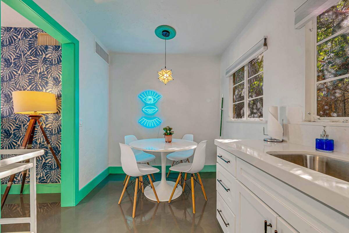 Round dining table with turquoise chairs beside white kitchen cabinetry.