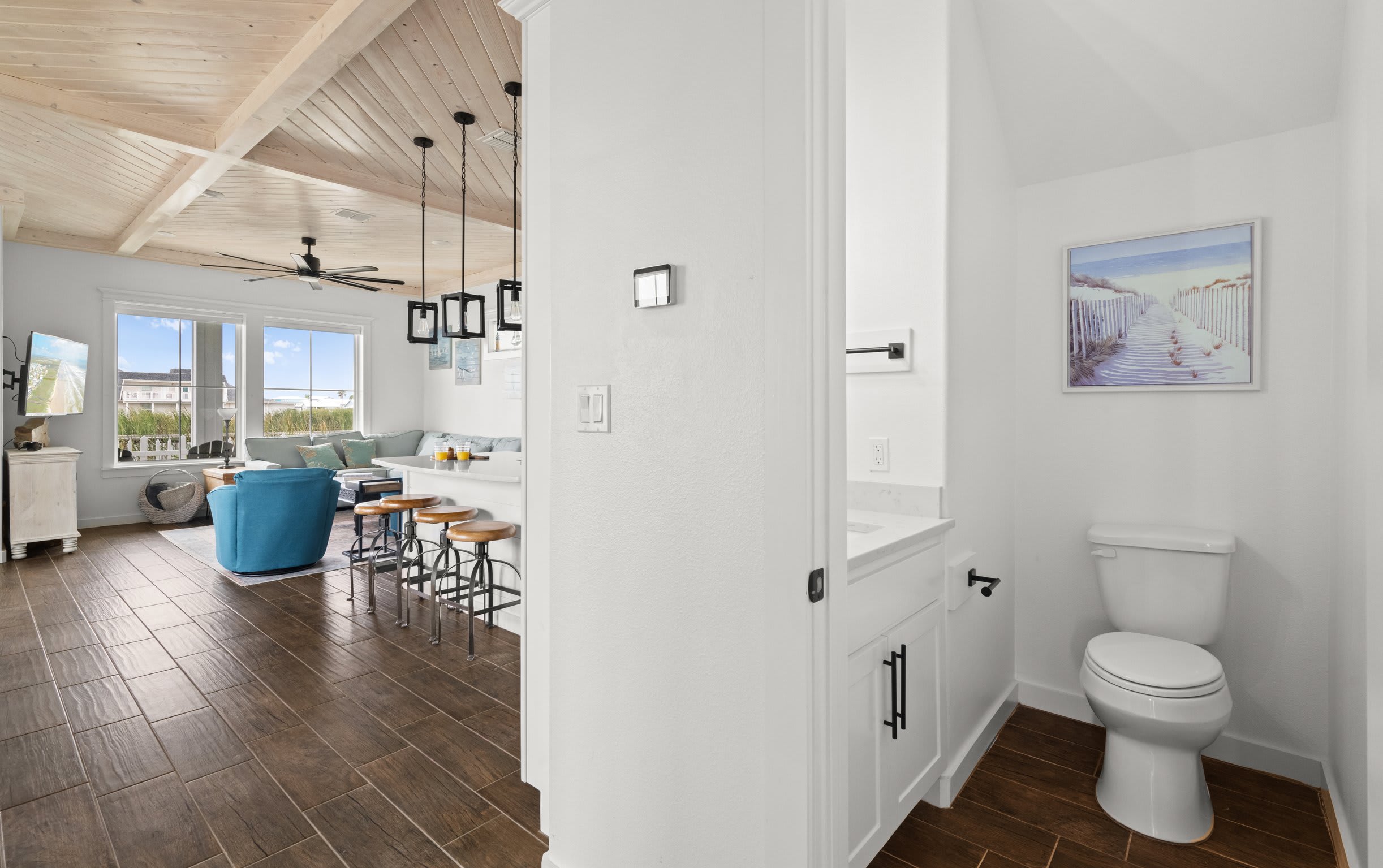 Half bath with white vanity, beach path art, and view to open living area