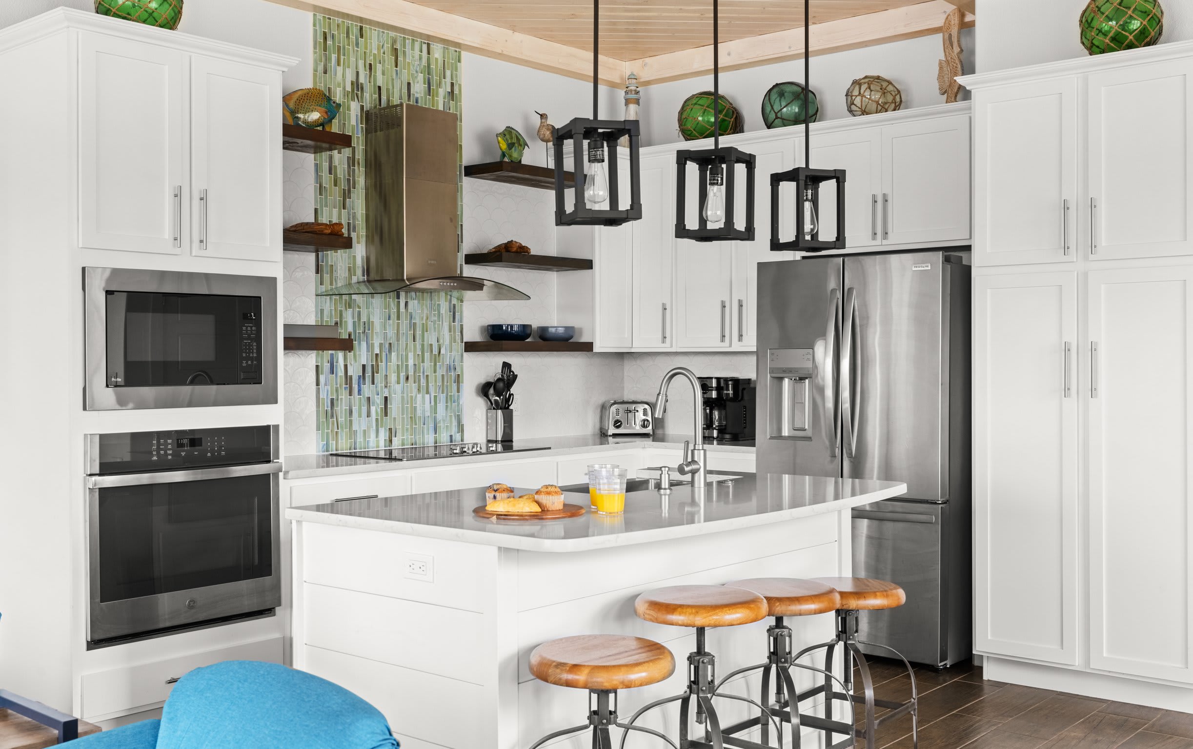 Kitchen with white cabinets, green mosaic backsplash, quartz island, and lantern pendants