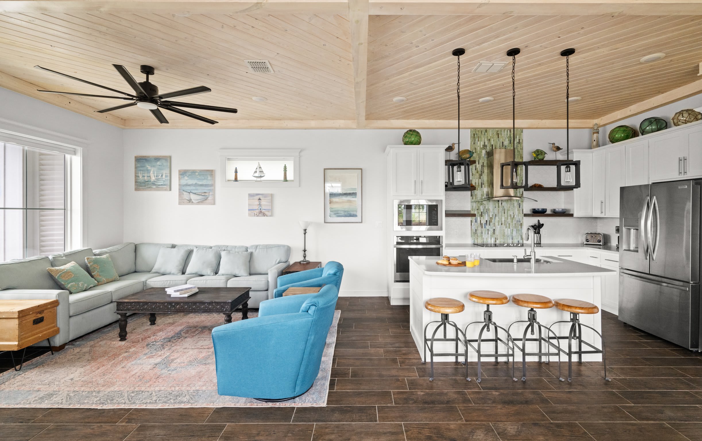 Open living and kitchen with sectional, blue swivel chairs, and sailing art gallery wall