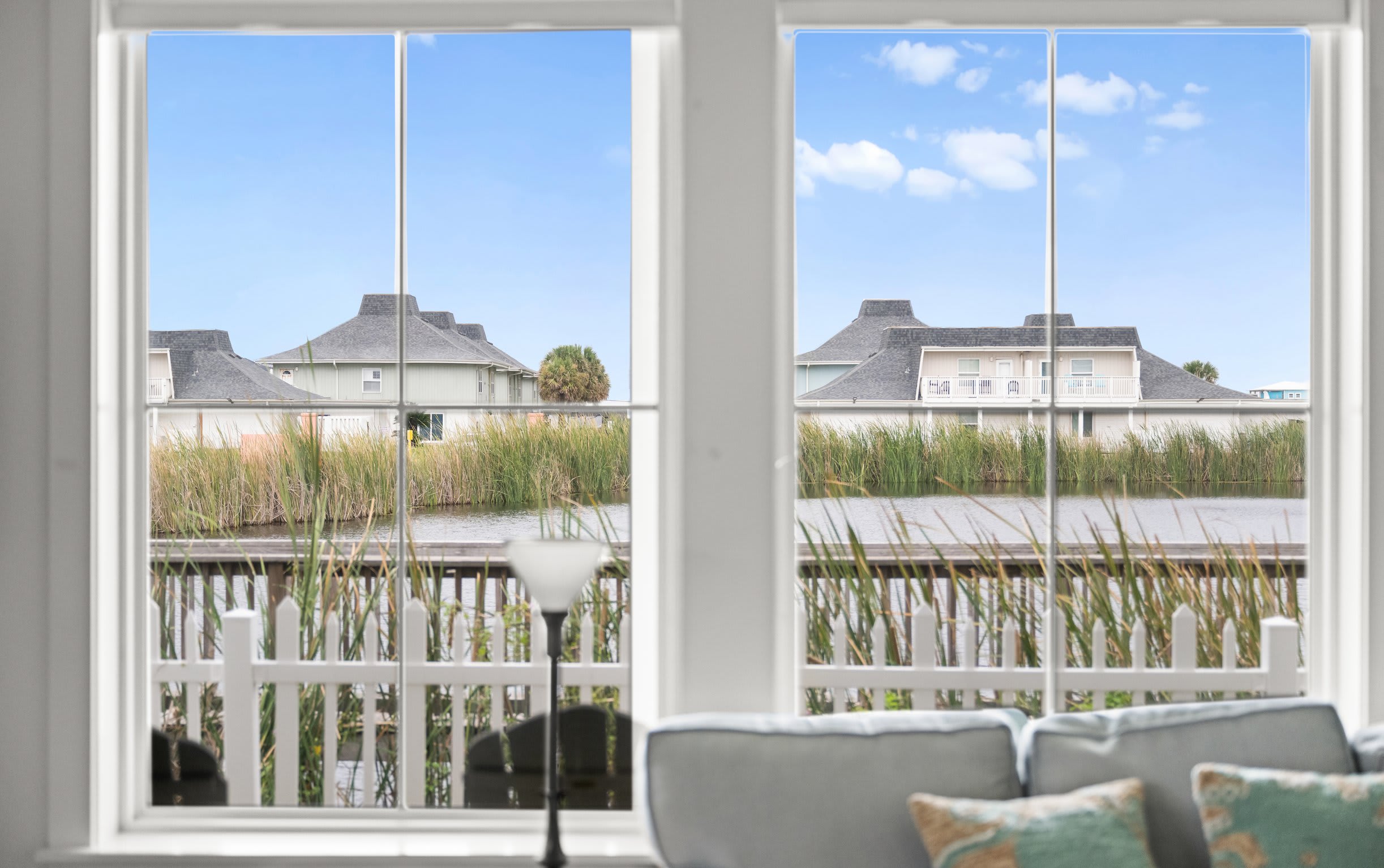 Window view of pond and marsh with reeds, white picket fence, and coastal homes
