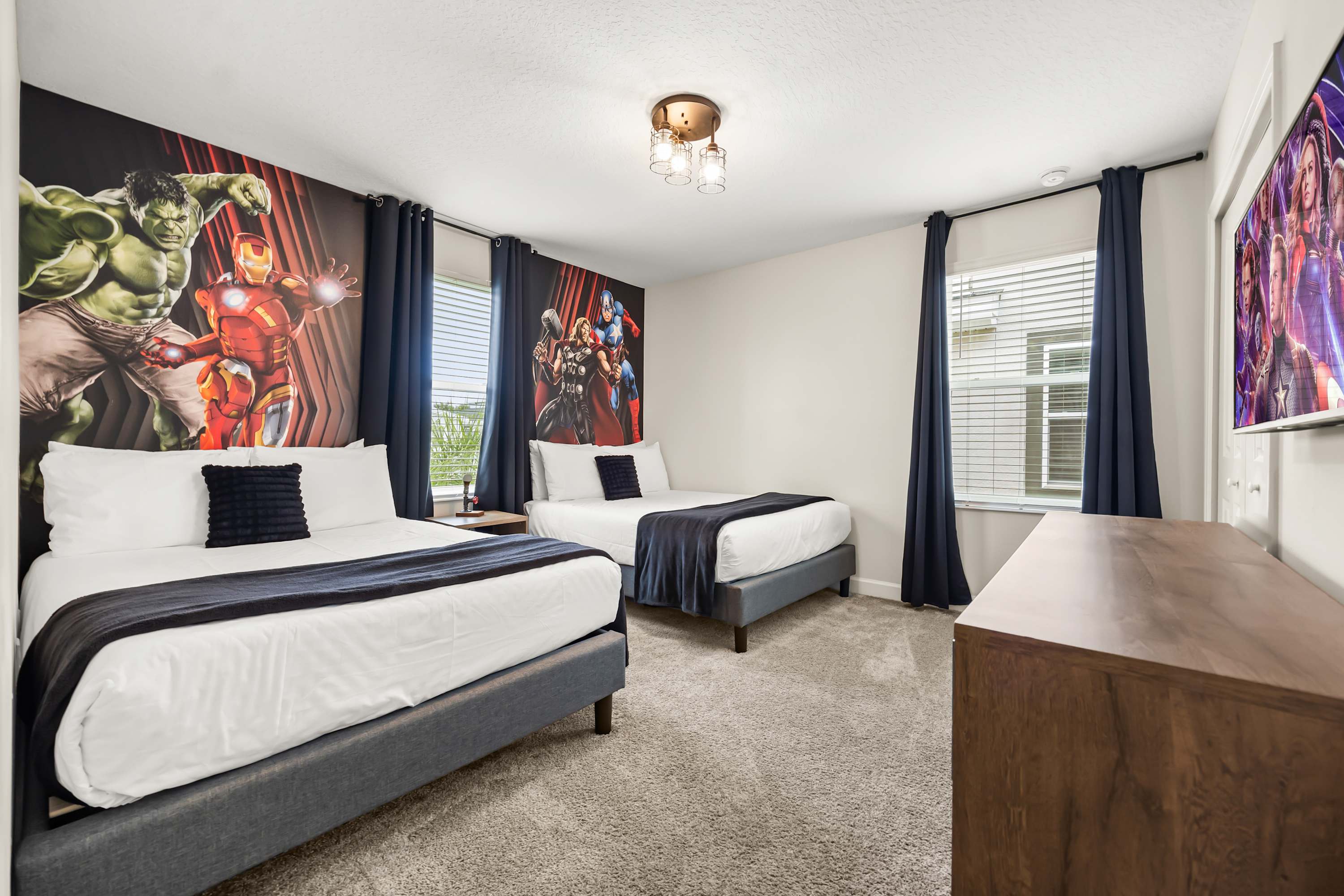 Avengers-themed bedroom with two double beds, bold wall art, and smart TV for entertainment.