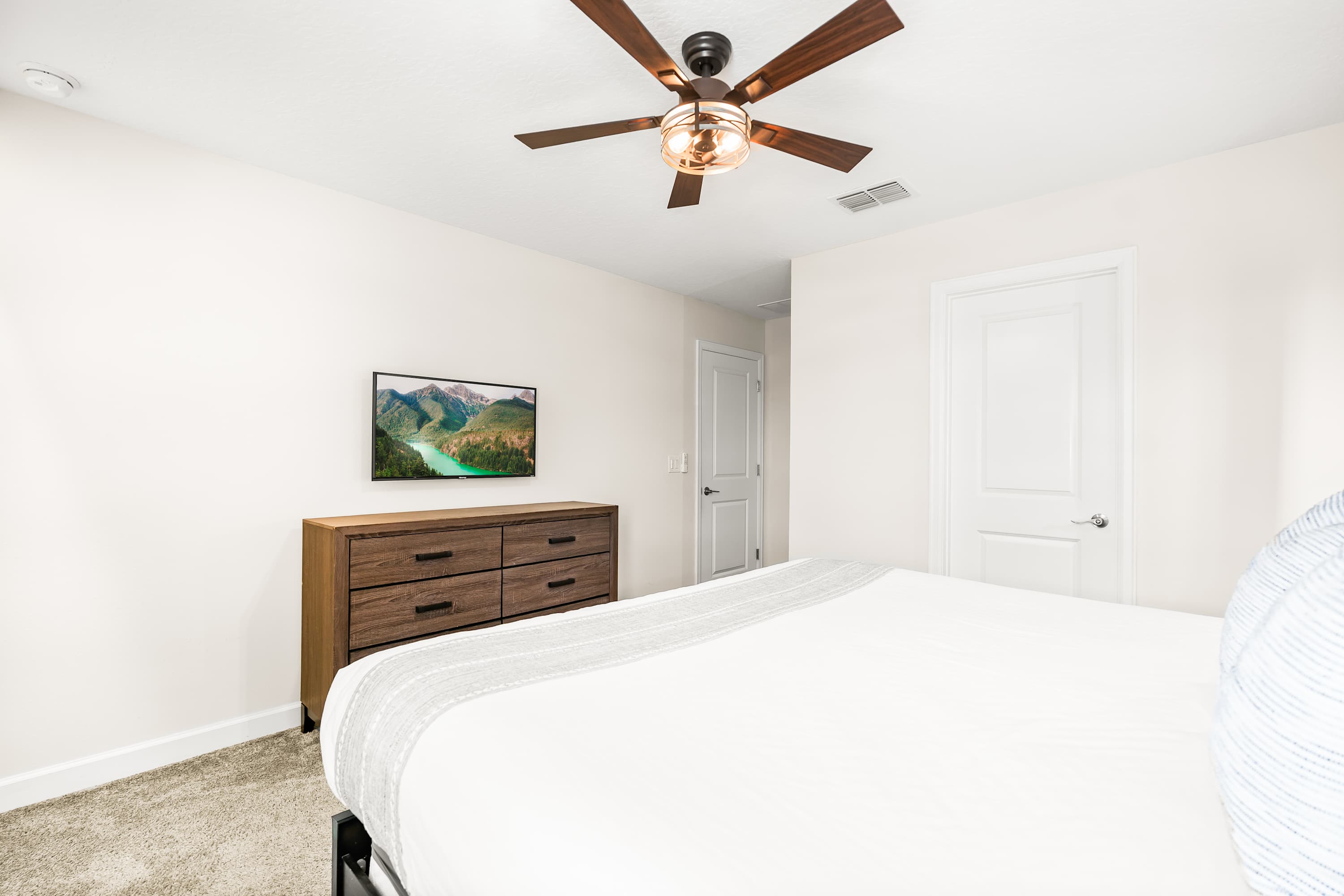 Spacious bedroom with clean design, ceiling fan, and TV for added comfort.