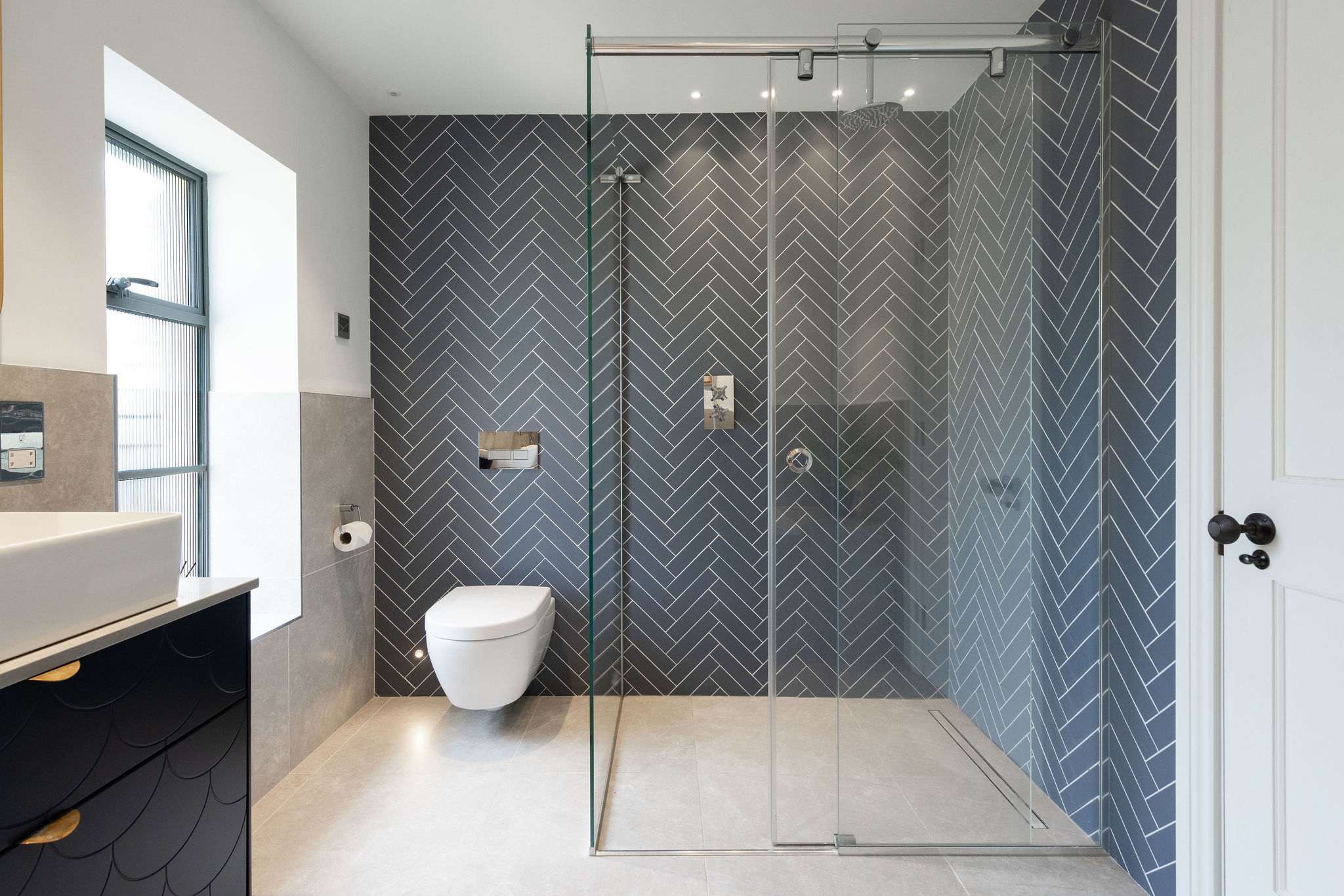 Striking herringbone-tiled walk-in shower with rainfall head, finished to the highest modern standard.