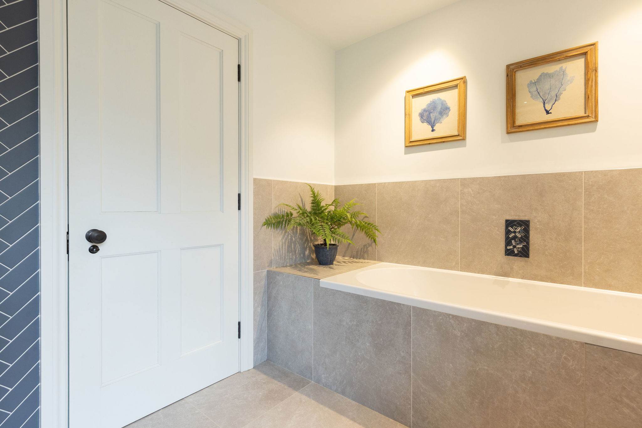 Relax in the elegant bathtub surrounded by natural stone tiles and charming coastal artwork.