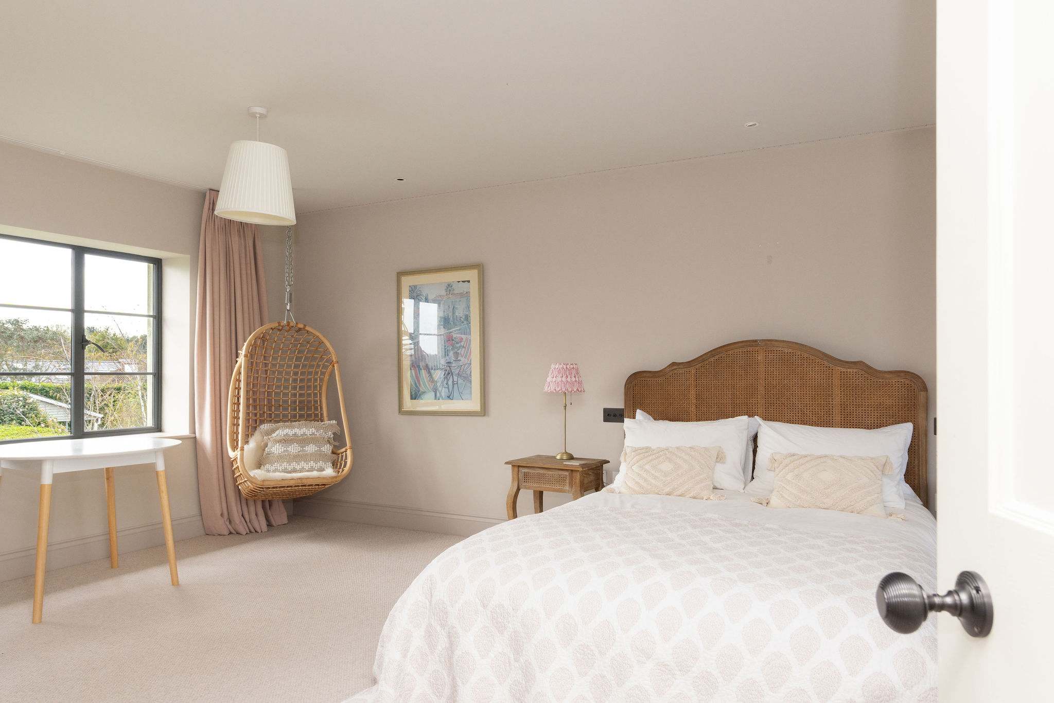 Charming double bedroom with a cosy hanging chair, soft tones, and garden views.