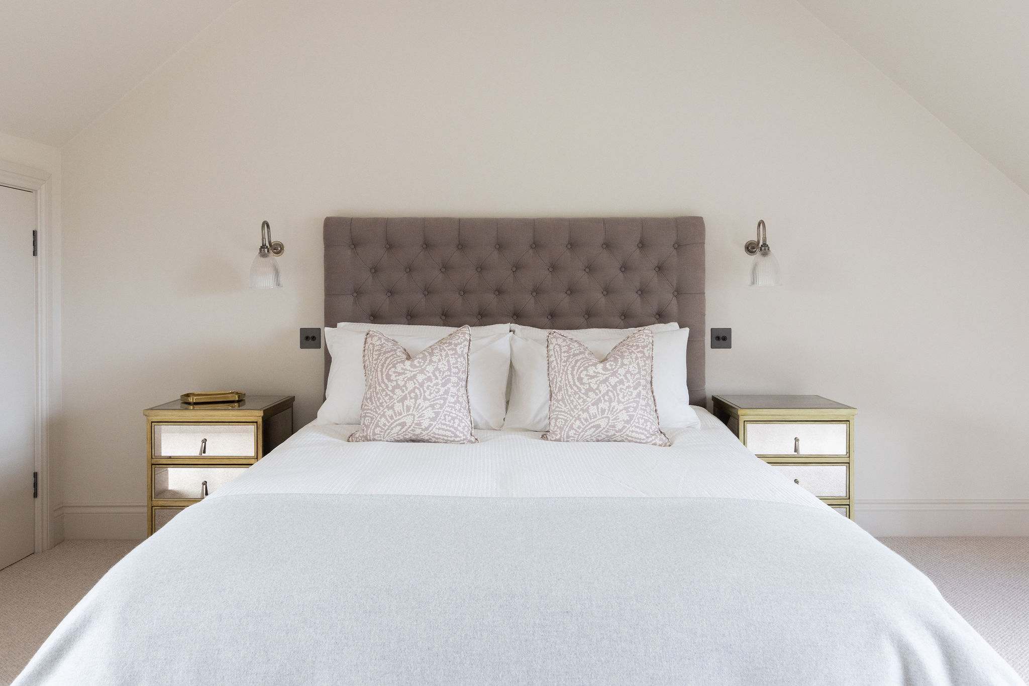 Luxurious king bedroom with tufted headboard, mirrored bedside tables, and crisp white linens.