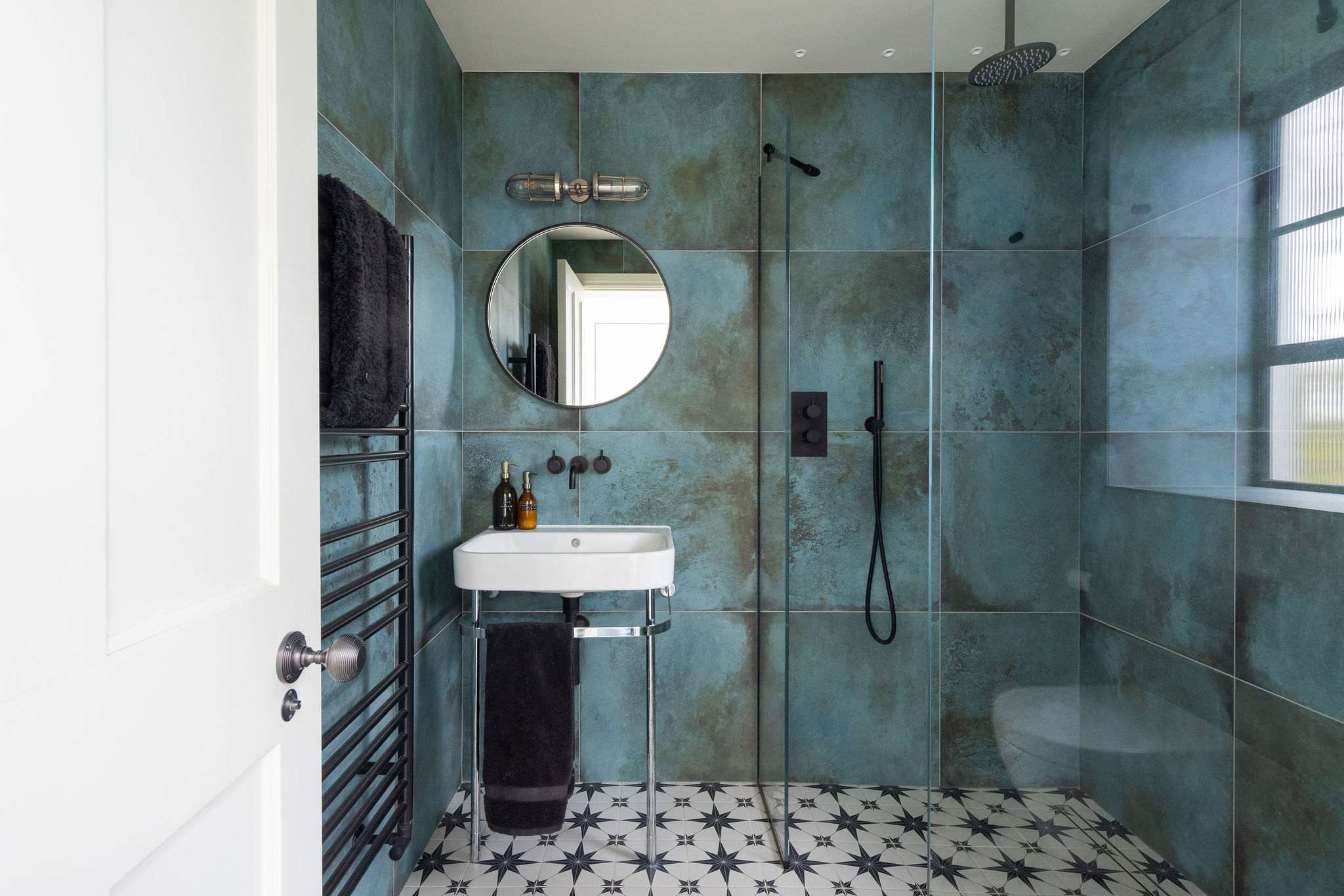 Bold teal-tiled shower room with patterned flooring, rainfall shower, and striking modern design.