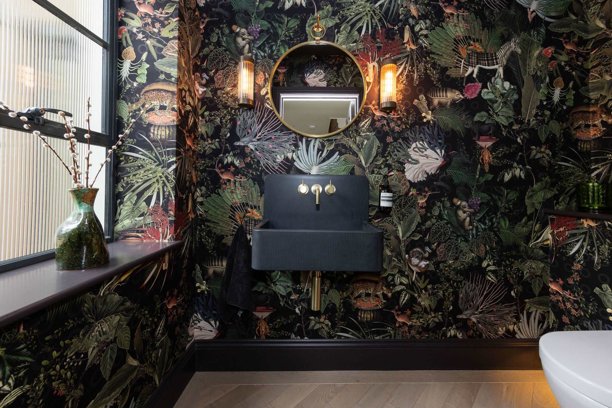 Show-stopping cloakroom featuring dramatic botanical wallpaper, gold accents, and bold designer flair.