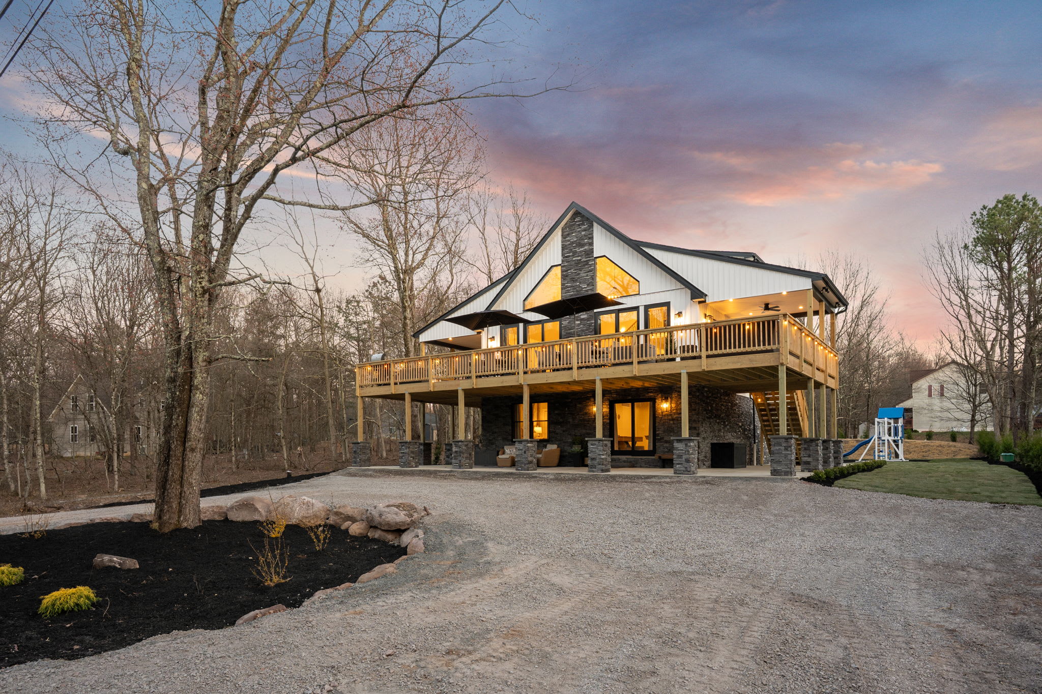 Welcoming front entrance with gravel drive and deck glowing at sunset