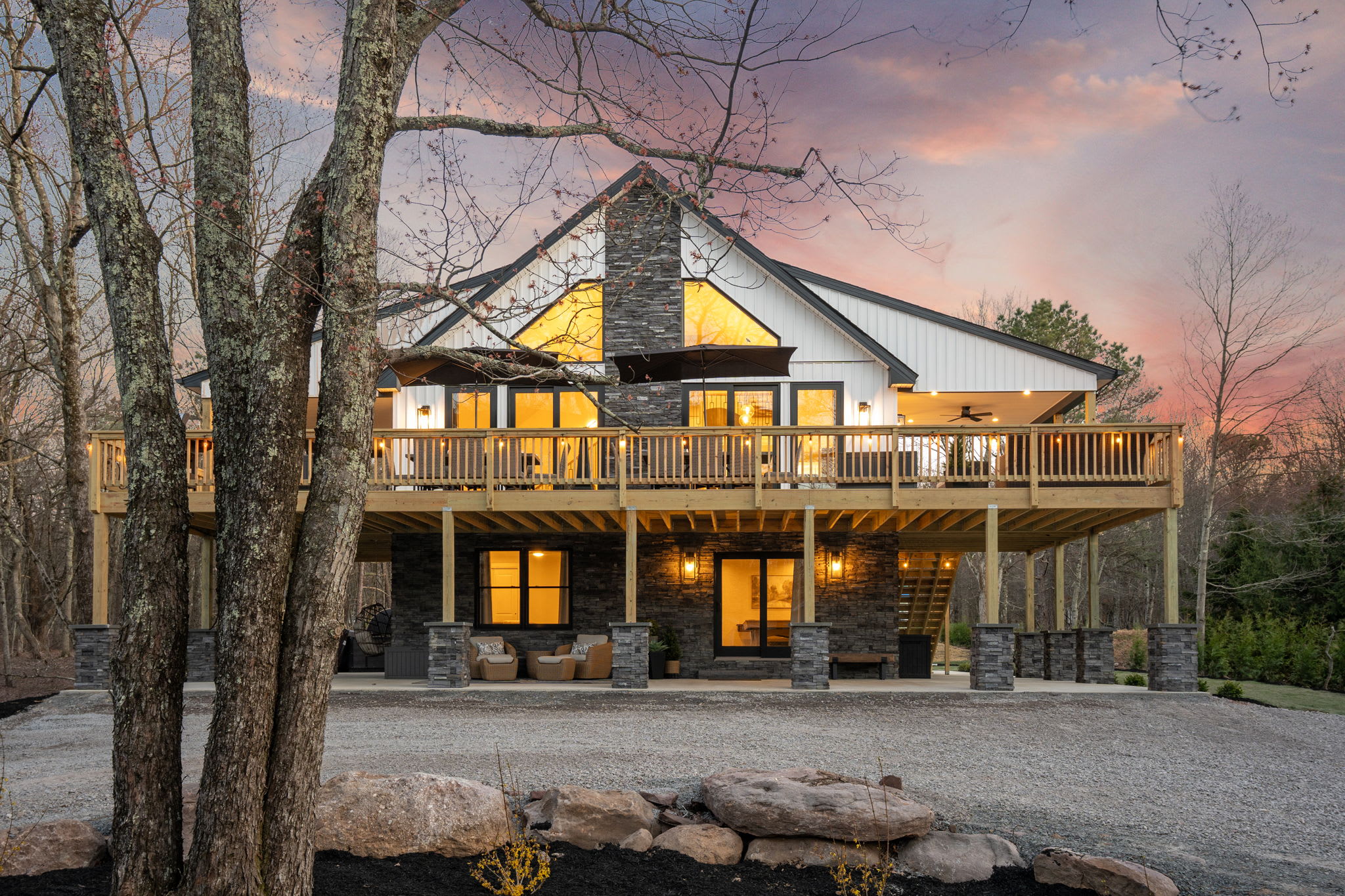 Twilight stone chimney exterior with warm windows and wraparound deck