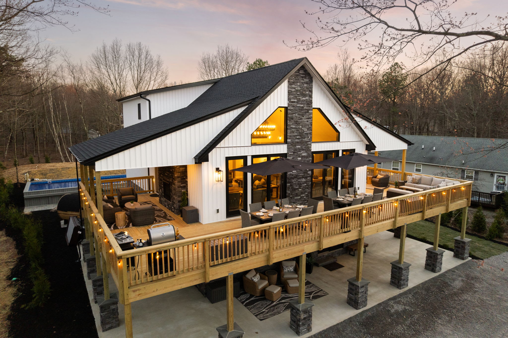 Three-story exterior at dusk with pool, deck, and barrel sauna nestled in the woods