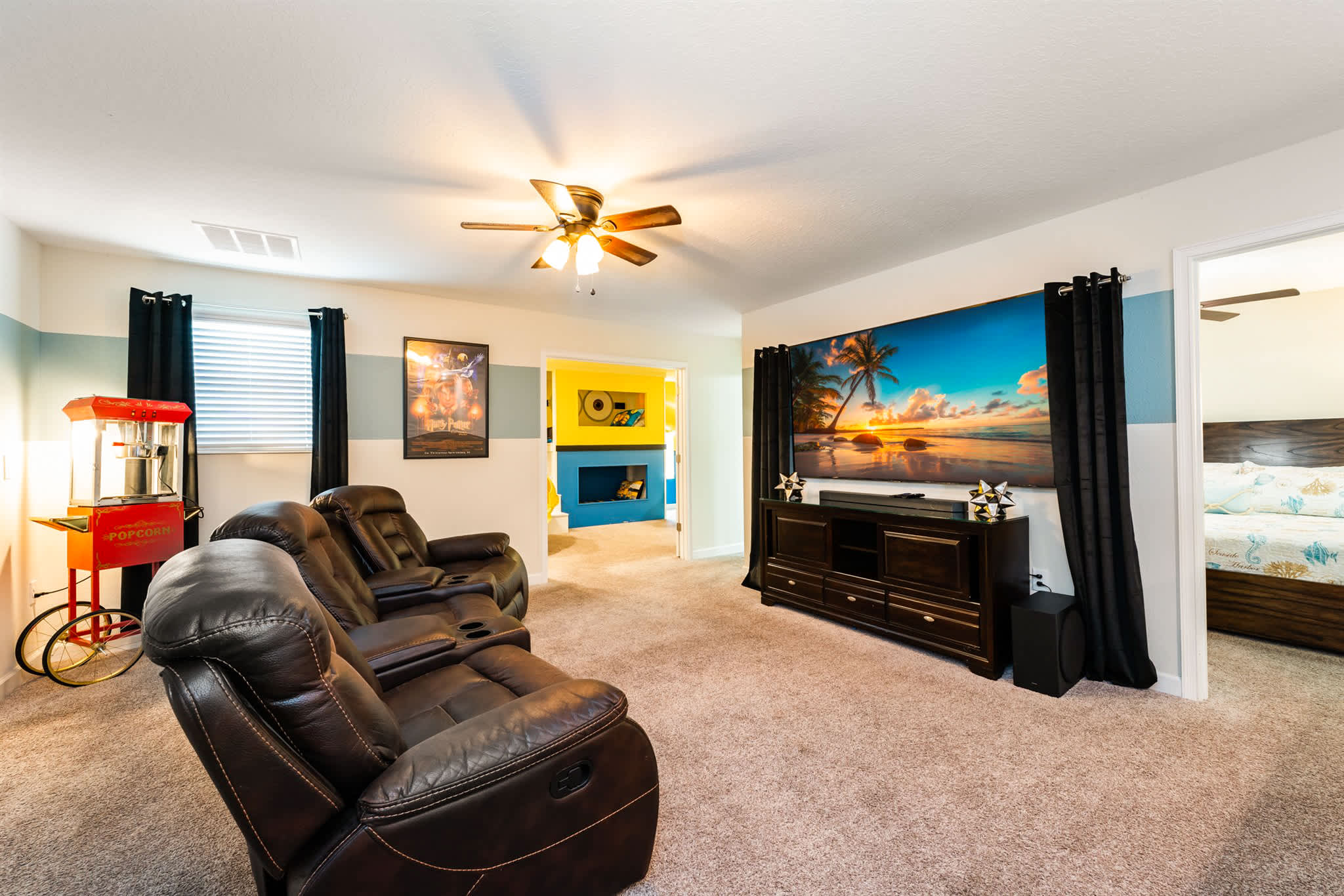 Private movie lounge with four leather recliners, a red popcorn machine, and tropical sunset wall art for memorable family film nights.