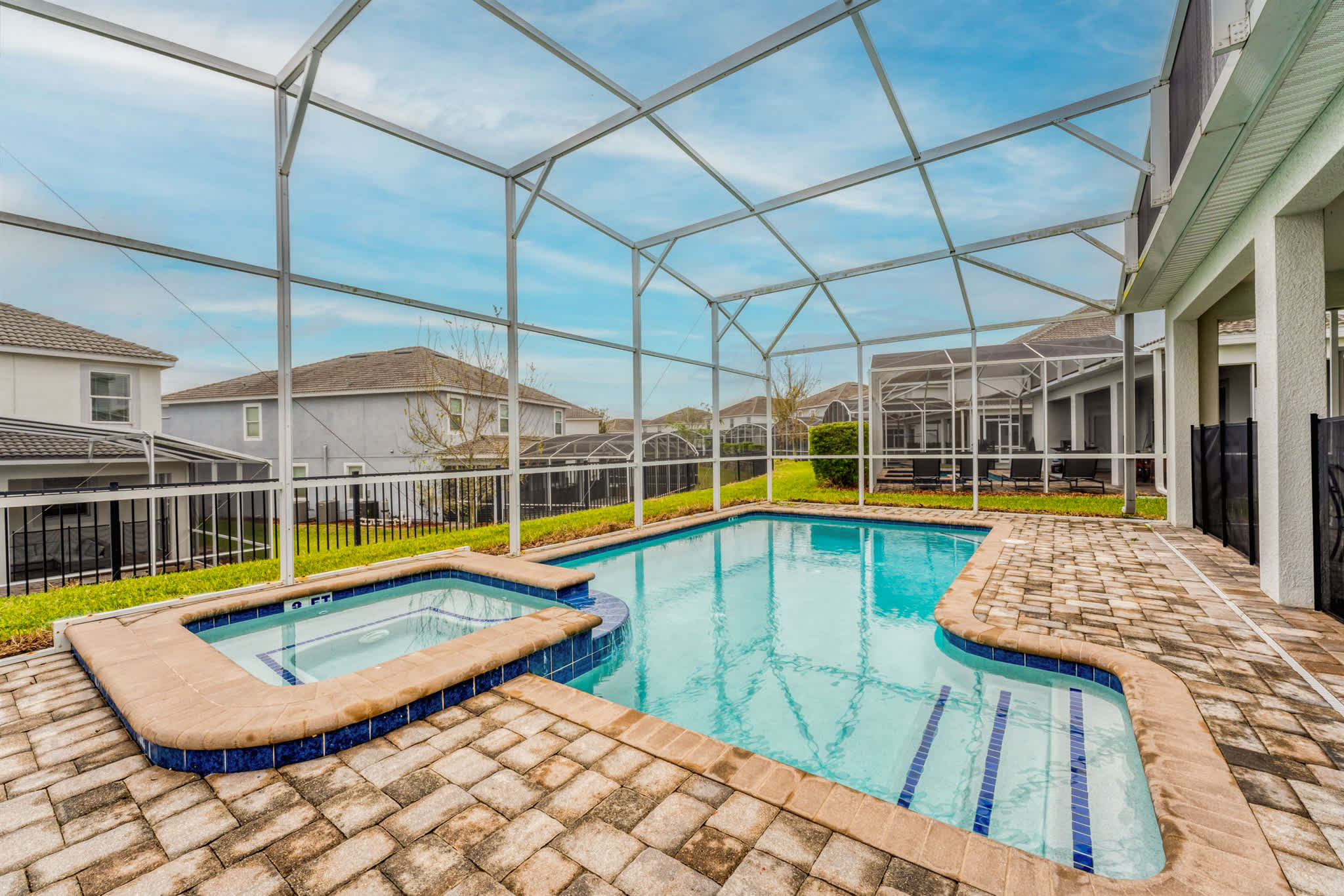 Resort-style screened pool and spa with sparkling blue water, spacious paver deck, and sunny private relaxation space.