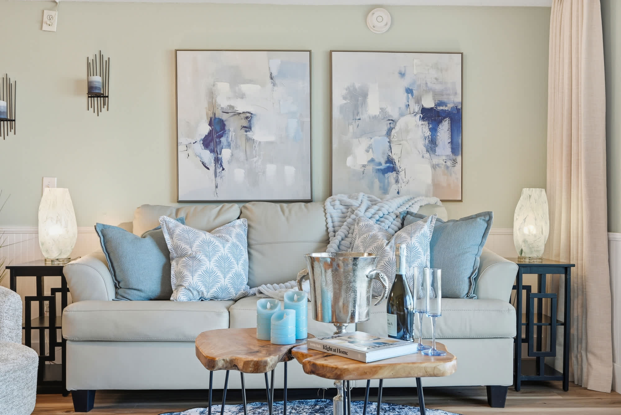 The Summit 131 – Comfortable living room with light-colored sofa, decorative pillows, abstract artwork, and wooden coffee tables.