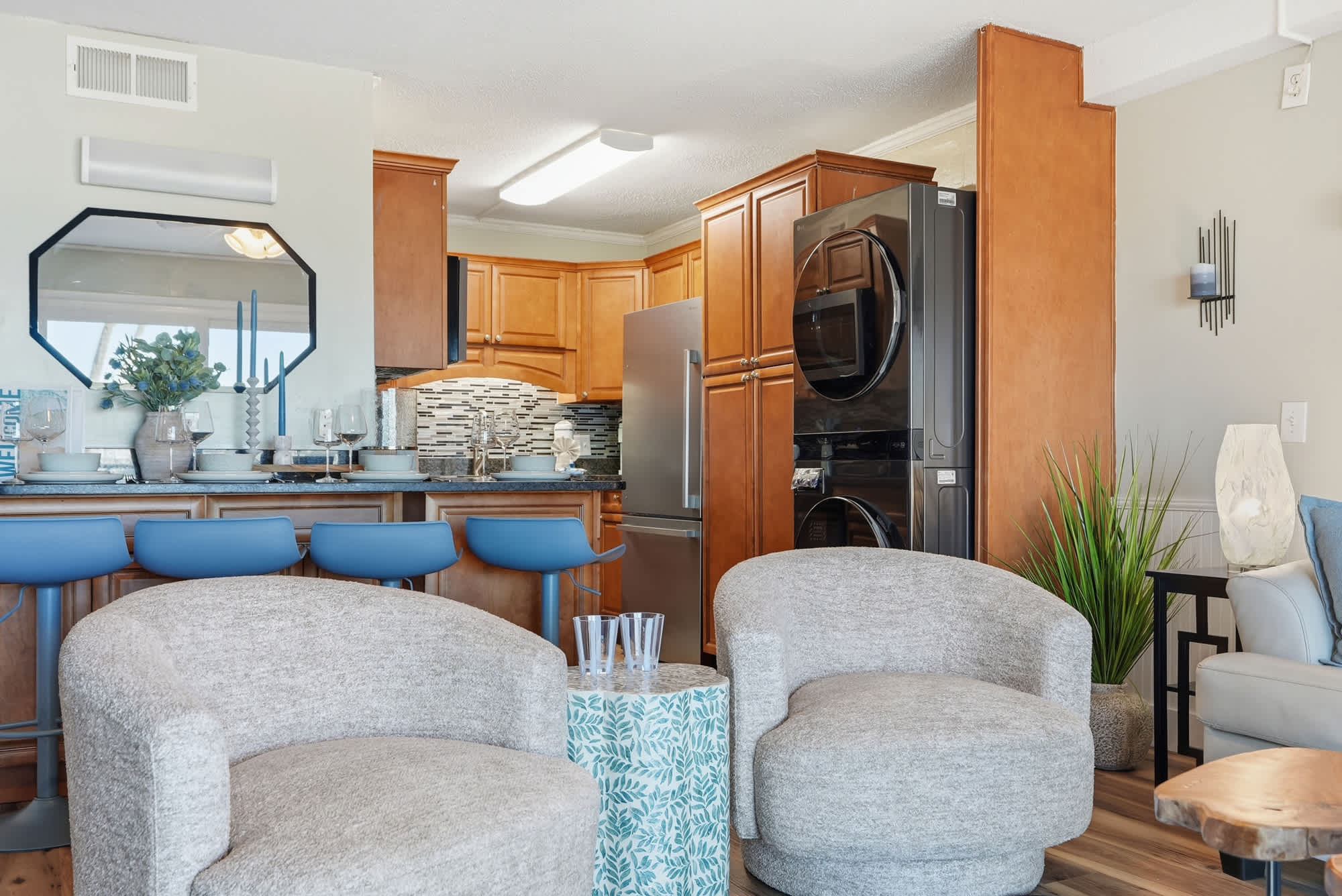The Summit 131 – Living room with modern kitchen, bar seating, and soft chairs; laundry appliances visible in background.