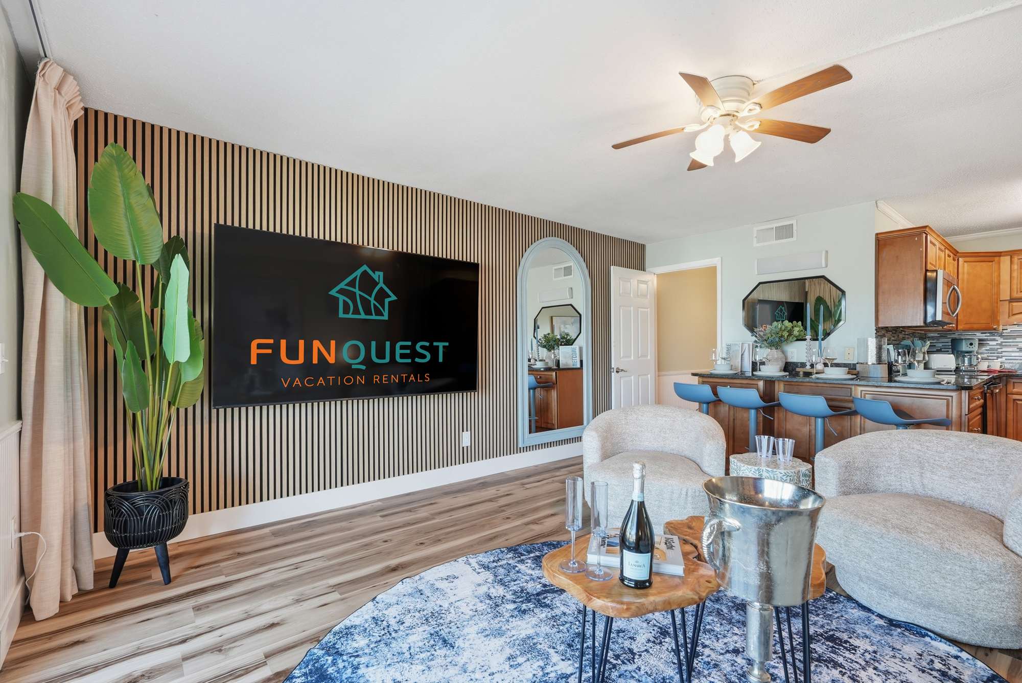 The Summit 131 – Living room with modern decor, large TV, two chairs, bar seating, and kitchen area.