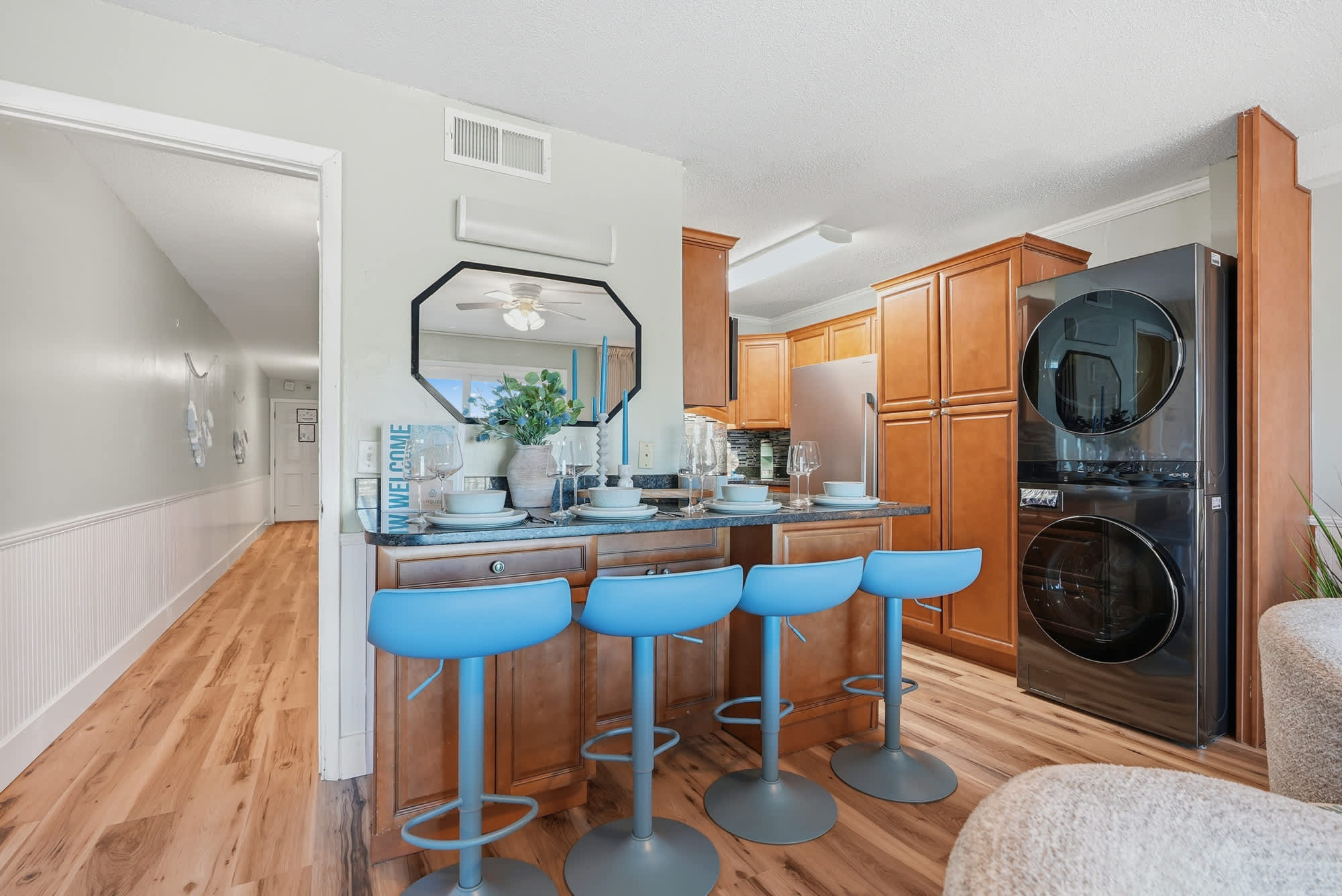 The Summit 131 – Modern kitchen with wooden cabinets, blue bar stools, and adjacent laundry appliances.
