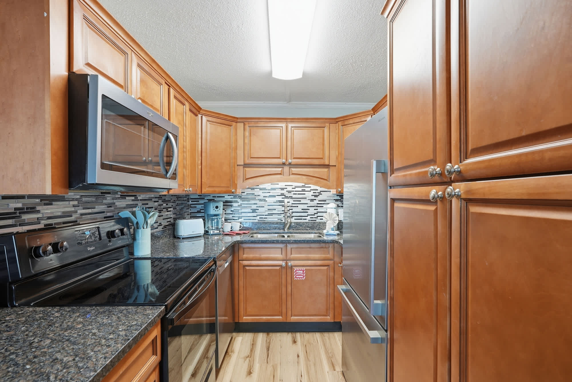 The Summit 131 – Modern kitchen with wooden cabinets, stainless steel appliances, granite countertops, and tile backsplash.