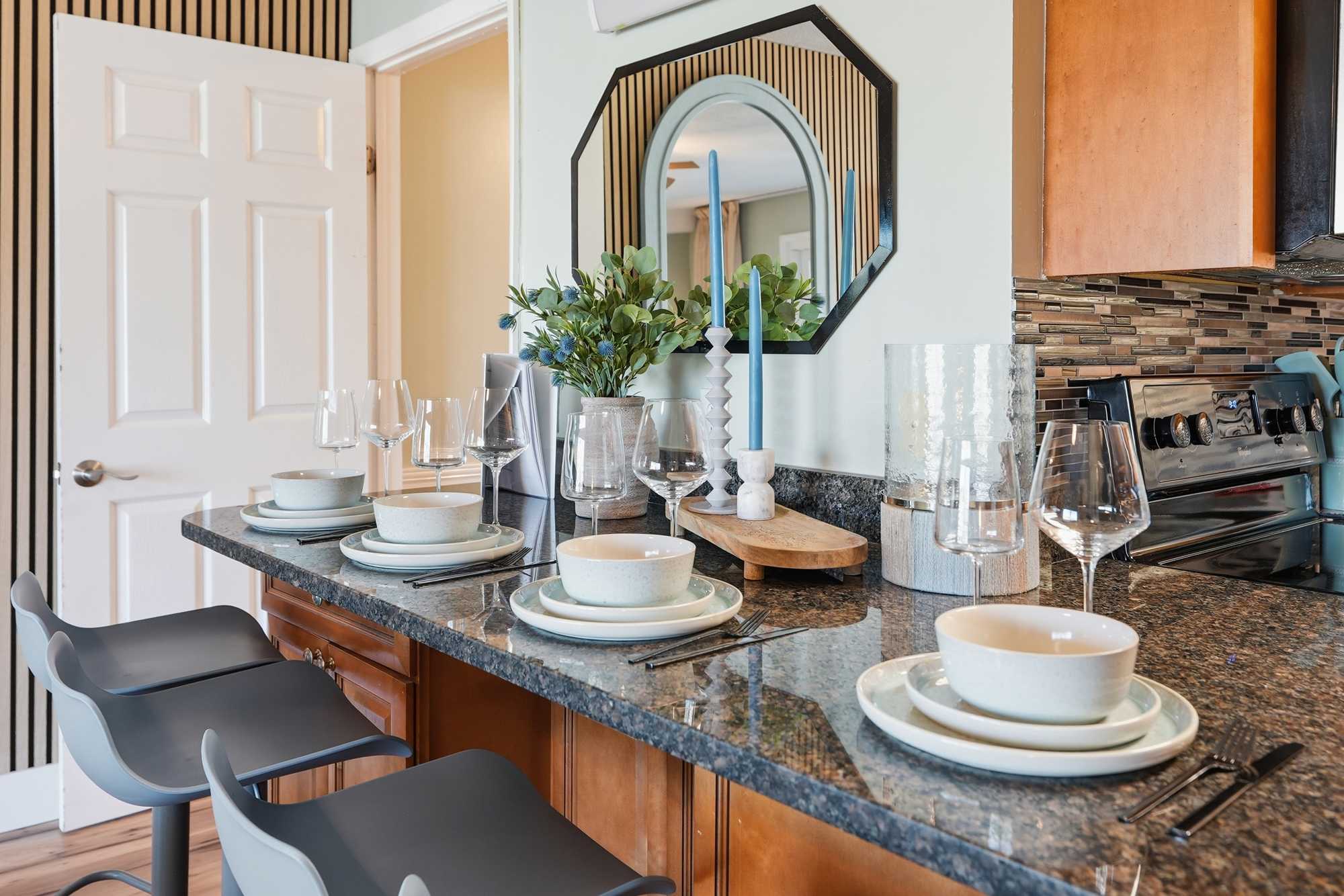 The Summit 131 – Kitchen bar with gray stools, tableware set, mirror, and decorative items.
