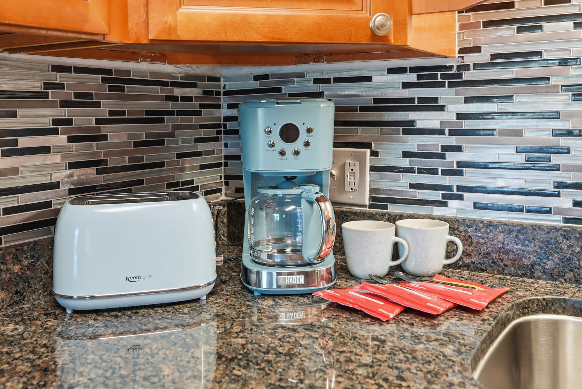 The Summit 131 – Kitchen counter with coffee maker, toaster, two mugs, and packets of coffee.