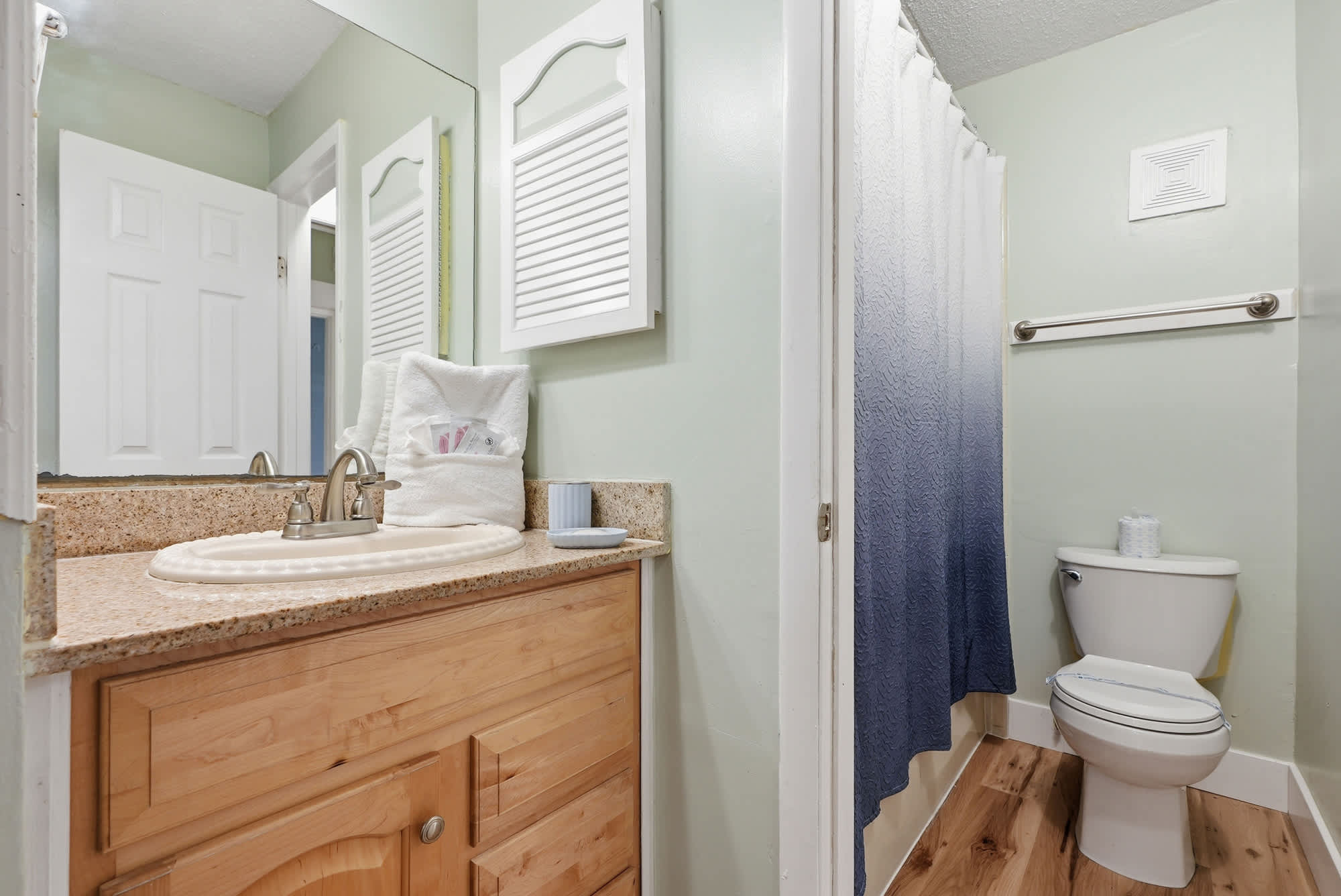 The Summit 131 – Bathroom with wood cabinet, sink, toilet, and shower curtain in gradient blue.