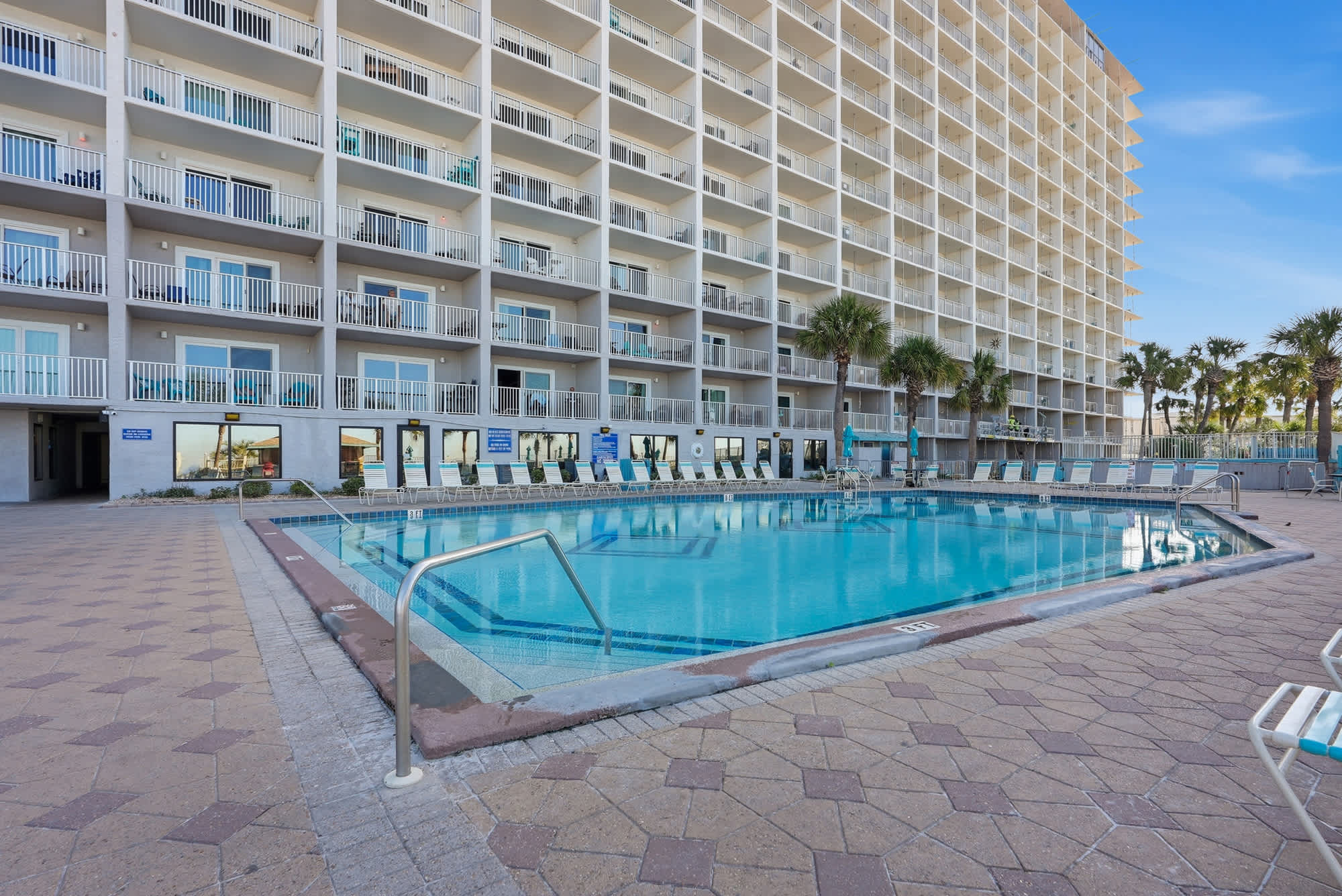 The Summit 131 – Swimming pool with lounge chairs and tall building balconies in the background. Palm trees nearby.