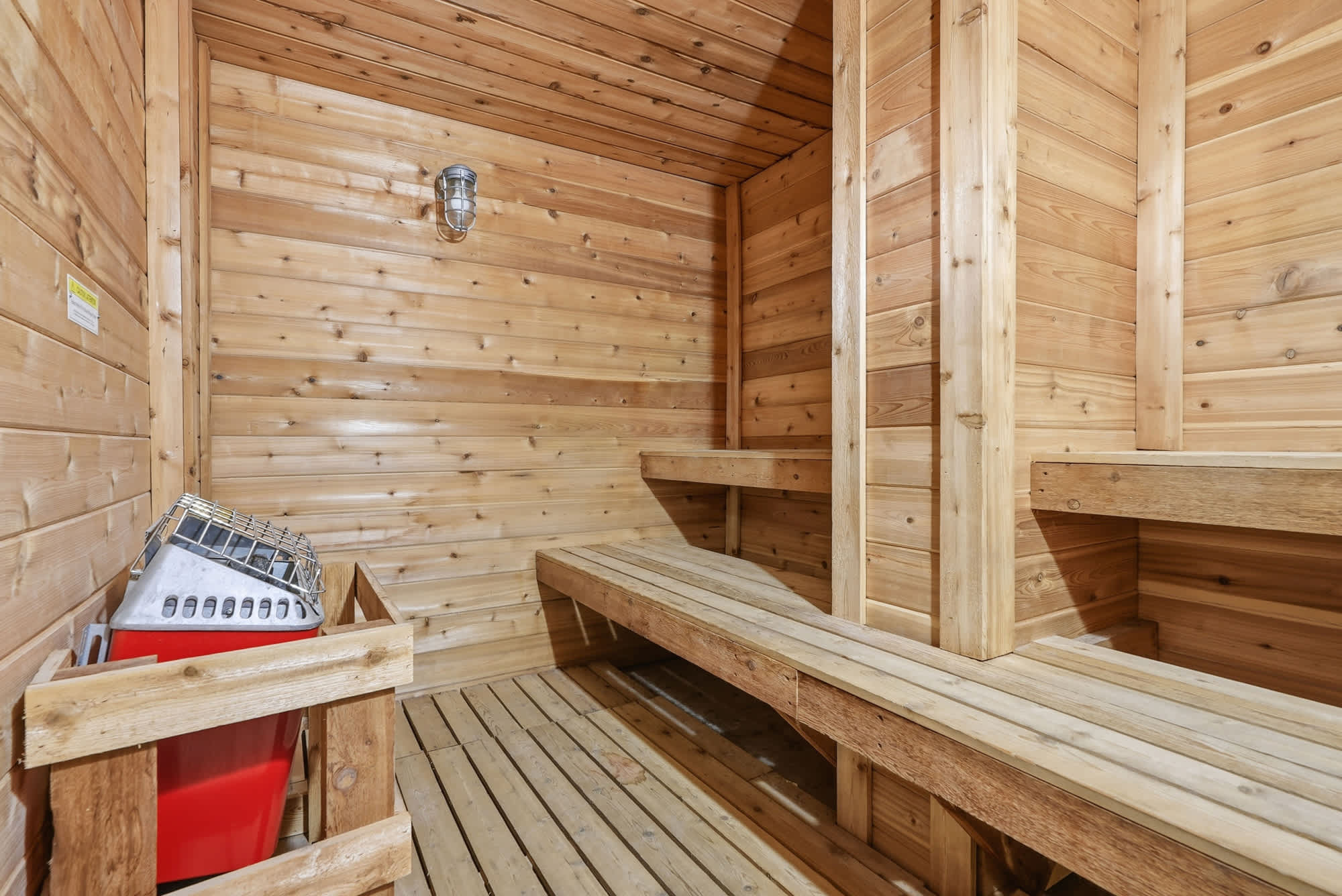 The Summit 1011 – Wood-paneled sauna with wooden benches and a red bin for accessories.