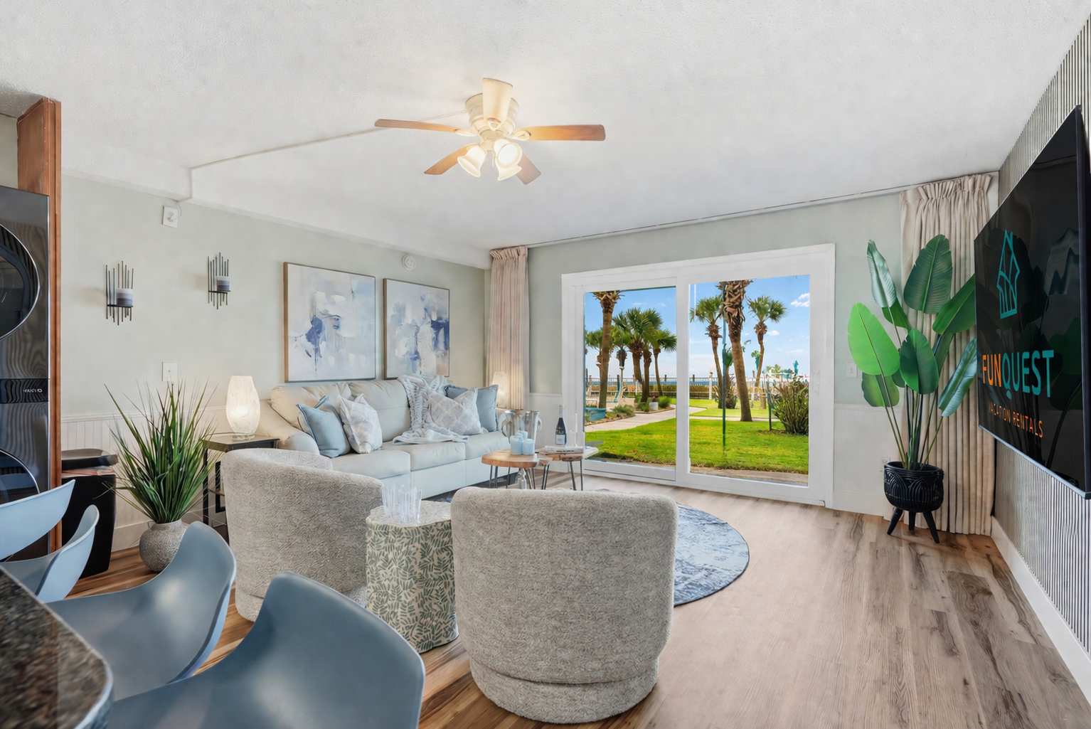 The Summit 131 – Living room with light furniture, palm tree view through large glass doors, and a TV mounted on the wall.