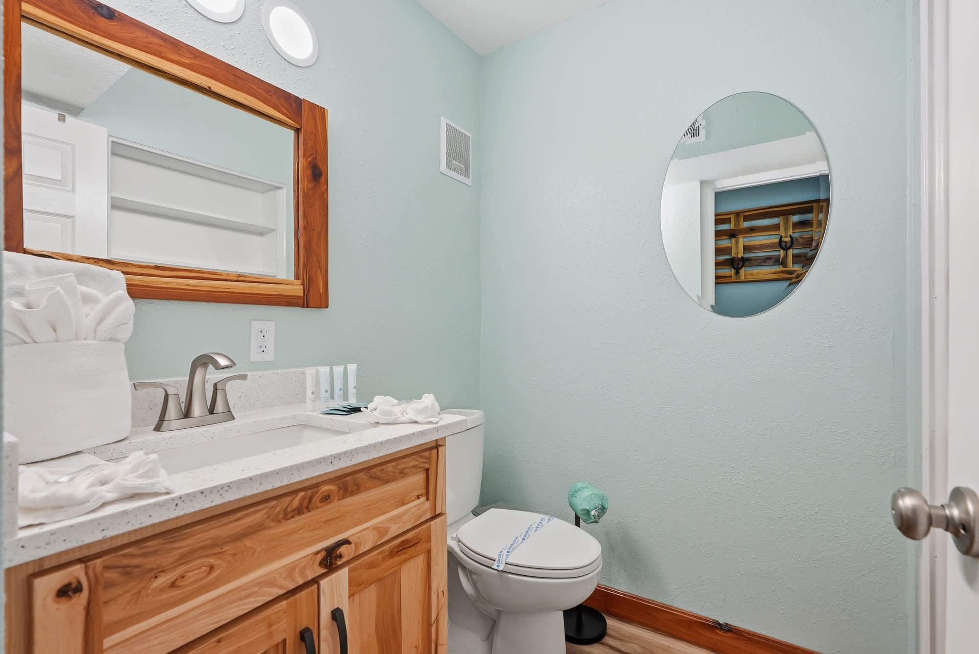 The Summit 206 – Modern bathroom with light blue walls, wooden cabinetry, a round mirror, and a toilet.