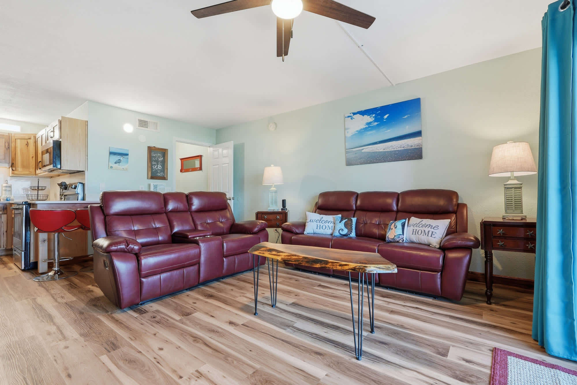 The Summit 206 – Living room with red leather sofas, wooden coffee table, and kitchenette in the background. Blue accent curtains.