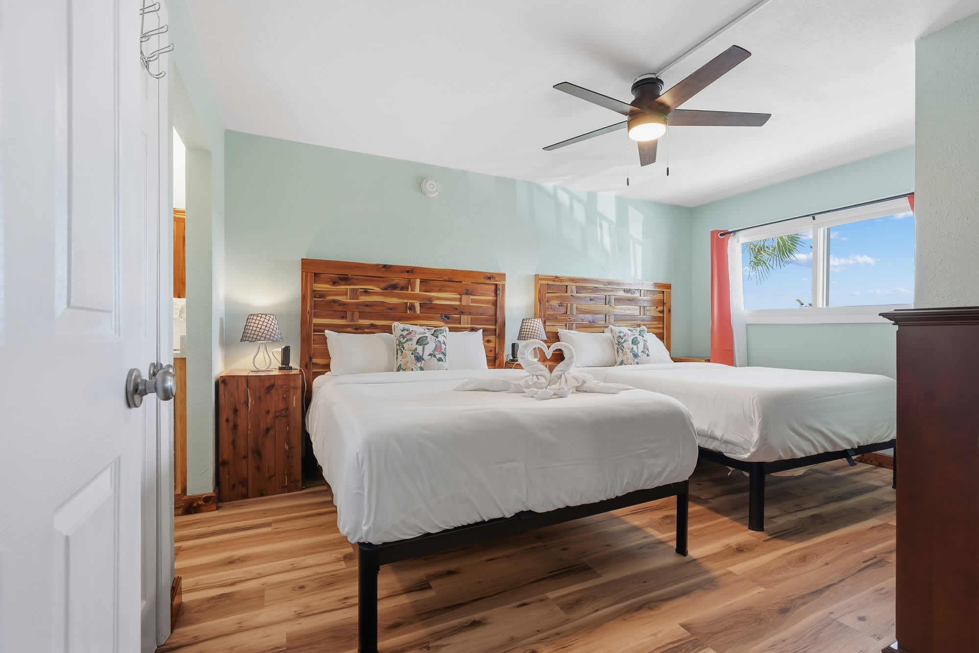 The Summit 206 – Bright guestroom with two beds, ceiling fan, wood accents, and window view of palm trees.