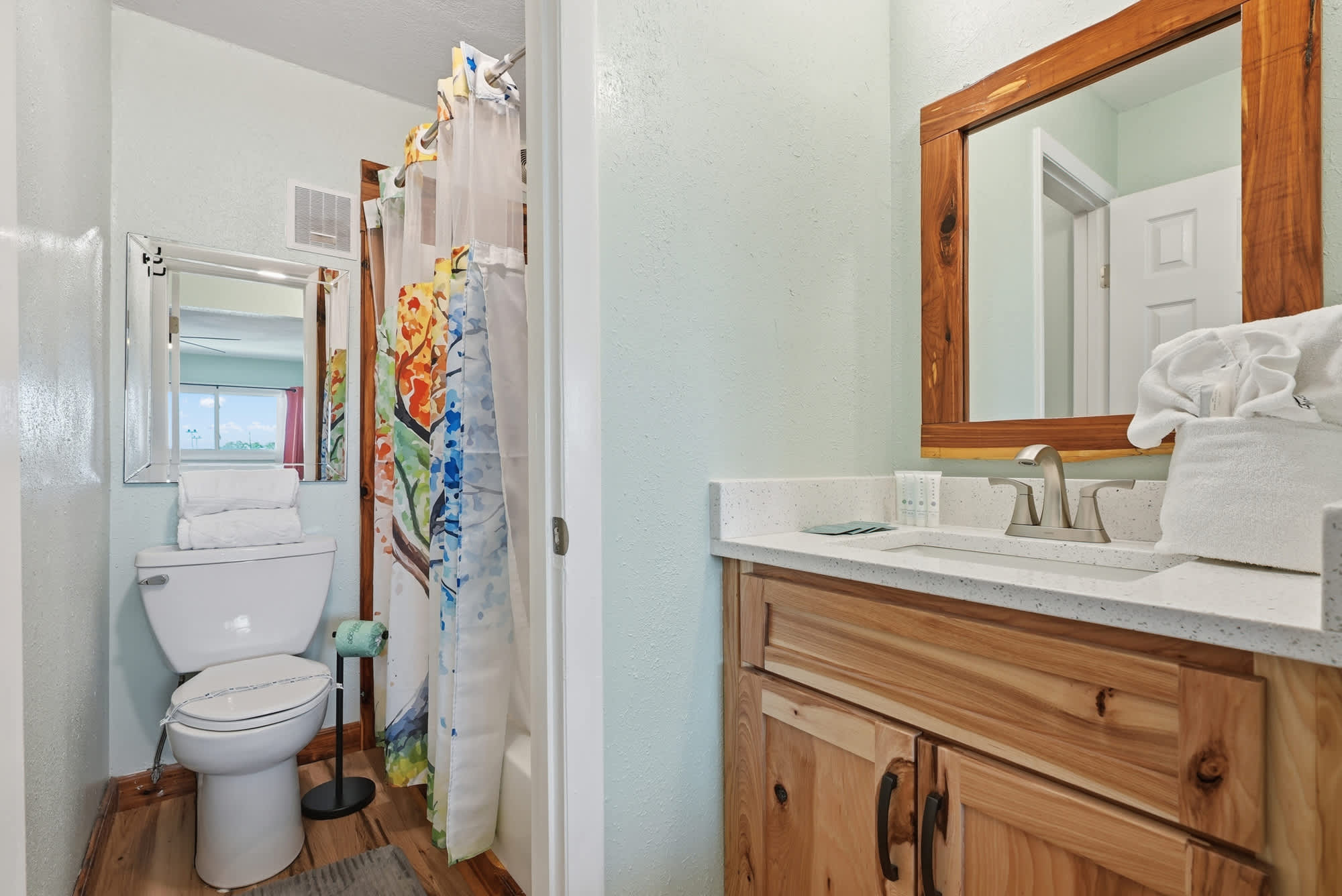 The Summit 206 – Bathroom with a toilet, shower curtain, sink with wooden cabinet, and mirror.