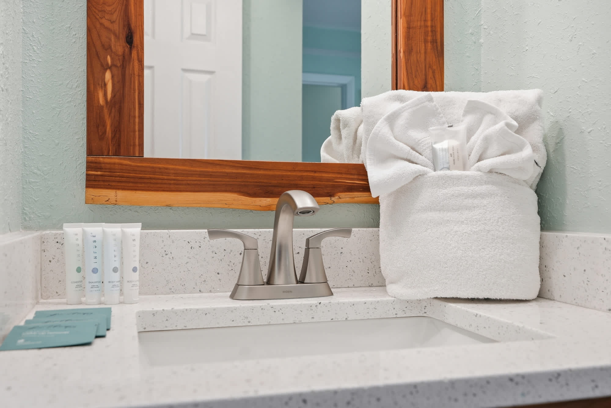 The Summit 206 – Bathroom vanity with sink, modern faucet, wooden mirror frame, towels, and toiletries on a countertop.