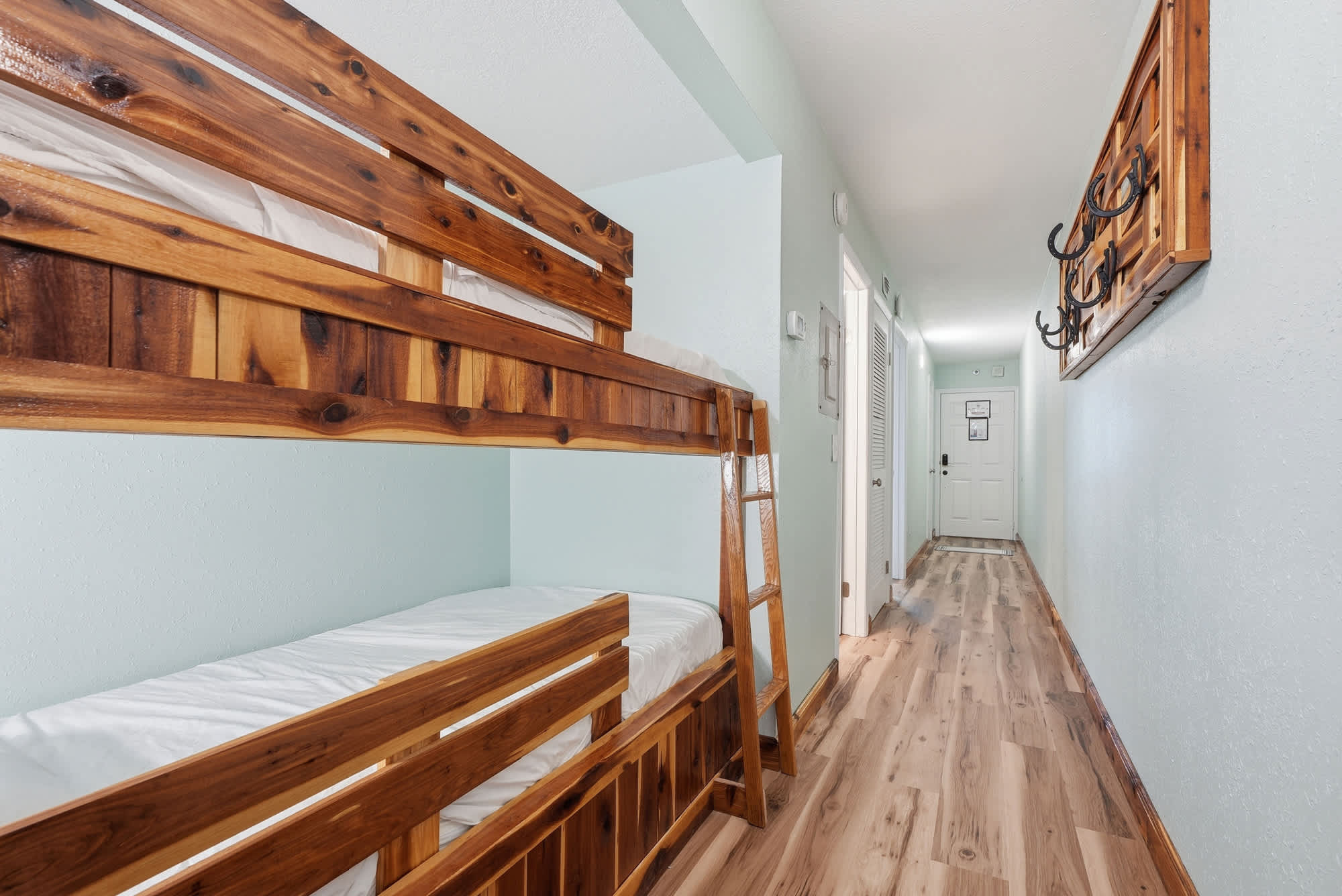 The Summit 206 – Bunk beds in a hallway with light blue walls and wooden flooring, leading to a door.