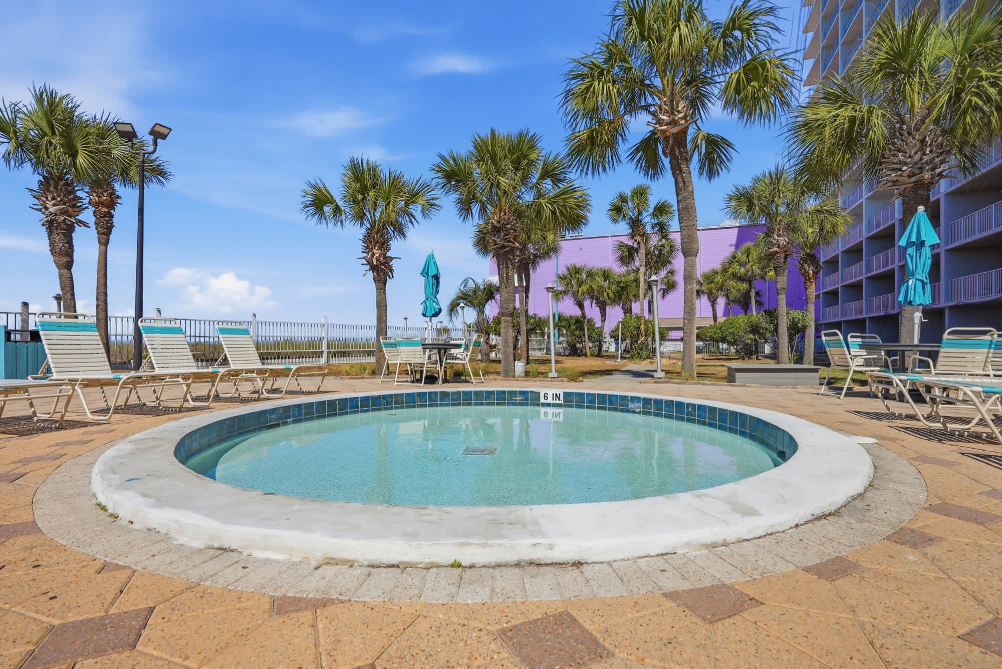 The Summit 206 – Hot tub surrounded by palm trees and lounge chairs, with a blue sky and nearby building visible.