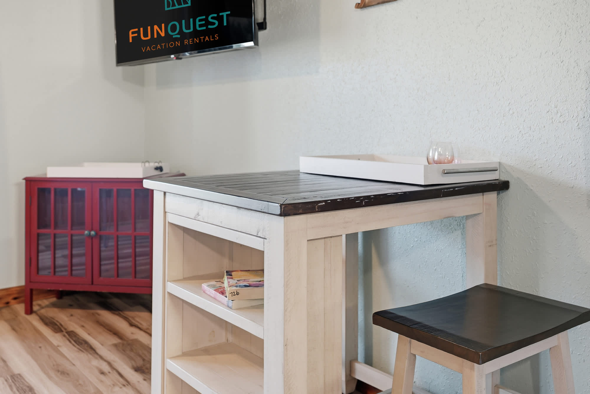 The Summit 206 – Dining table with a stool, red cabinet, and wall-mounted TV in a light-colored room.