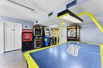 The Summit Penthouse 1501 – Game room featuring air hockey table and arcade machines, with tiled flooring and light blue walls.