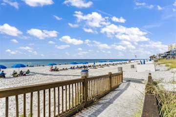 The Summit 726 – Beach view with umbrellas, sandy area, wooden walkway, and a clear blue sky.