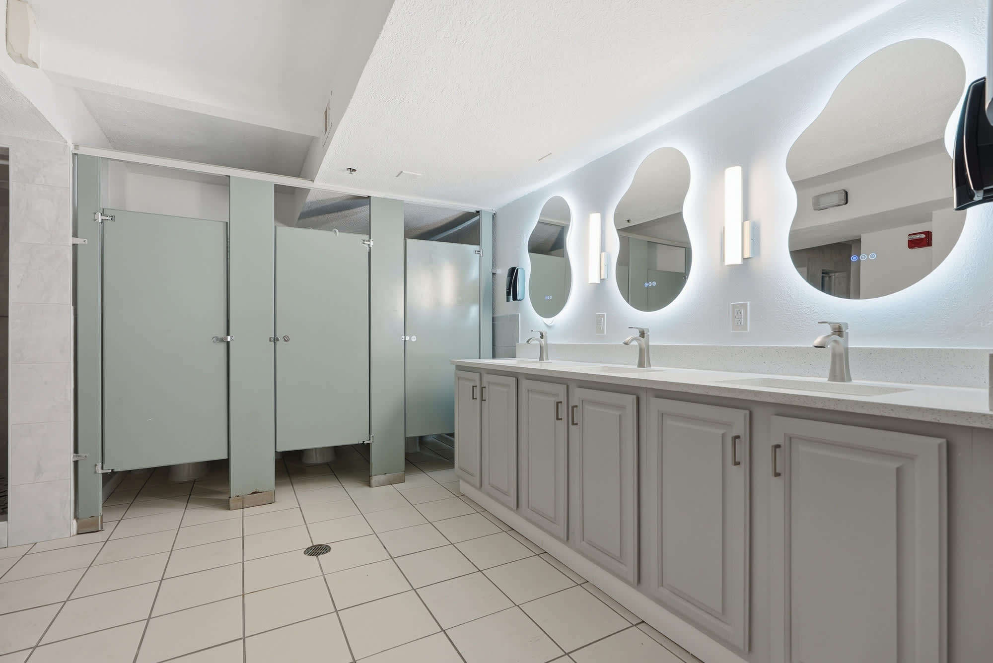 The Summit 615 – Bathroom with two sinks, large mirrors, and three shower stalls with green doors.