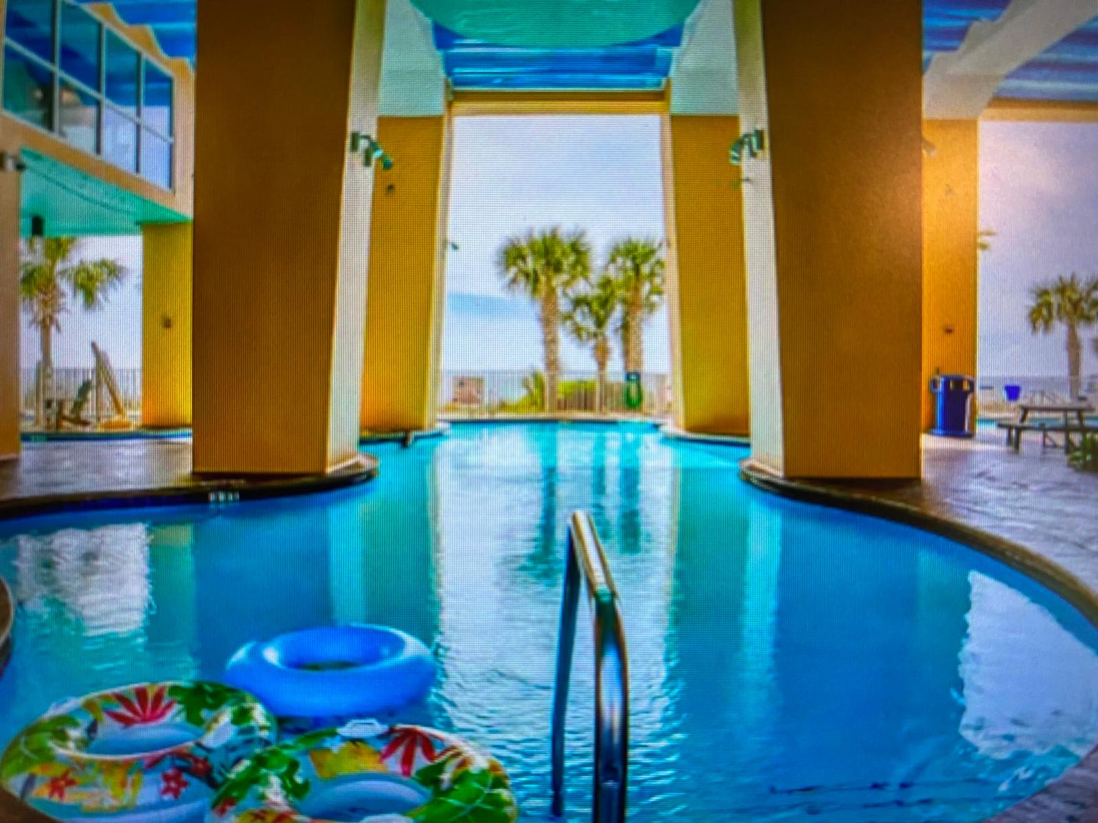 Splash 804E – Indoor pool area with two float rings and a view of palm trees outside.