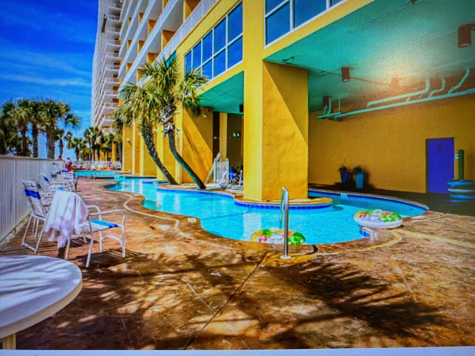 Splash 804E – Pool area with colorful floats, lounge chairs, and palm trees against a bright yellow building.