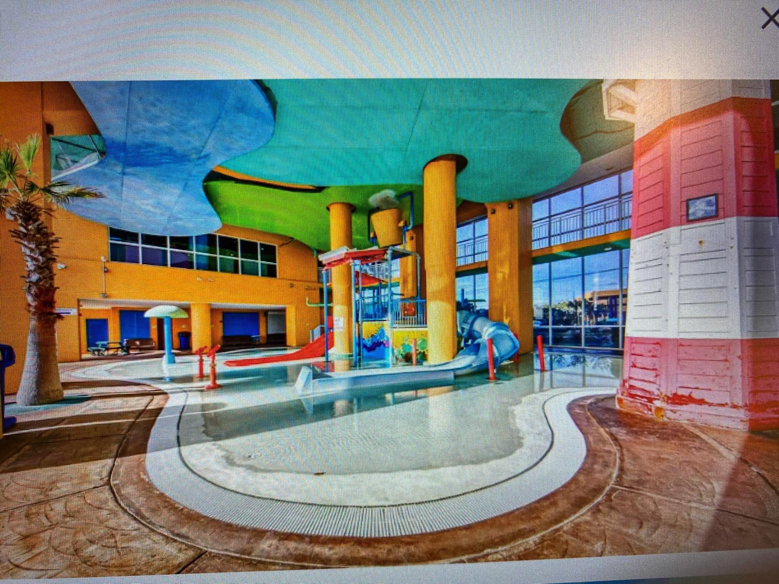 Splash 804E – Indoor water park area with colorful slides, palm trees, and large windows showcasing an outdoor view.