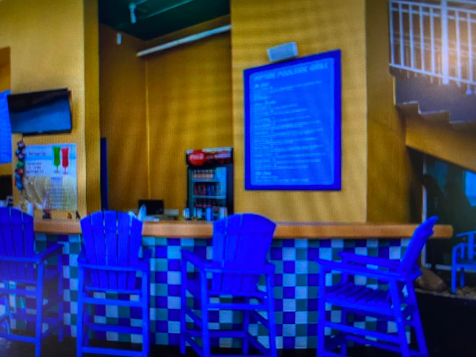 Splash 804E – Colorful poolside bar with blue chairs and a menu board on a yellow wall.